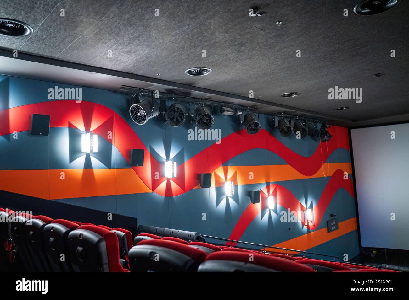 A modern cinema auditorium with a vibrant abstract wall design and rows ...
