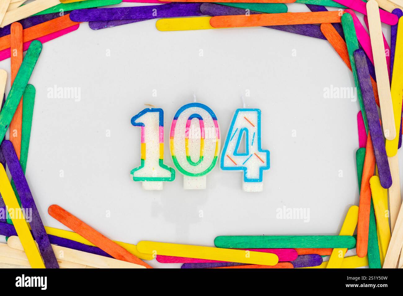 Candles in shape of the number 104 in popsicle colorful sticks frame isolated on white background Stock Photo