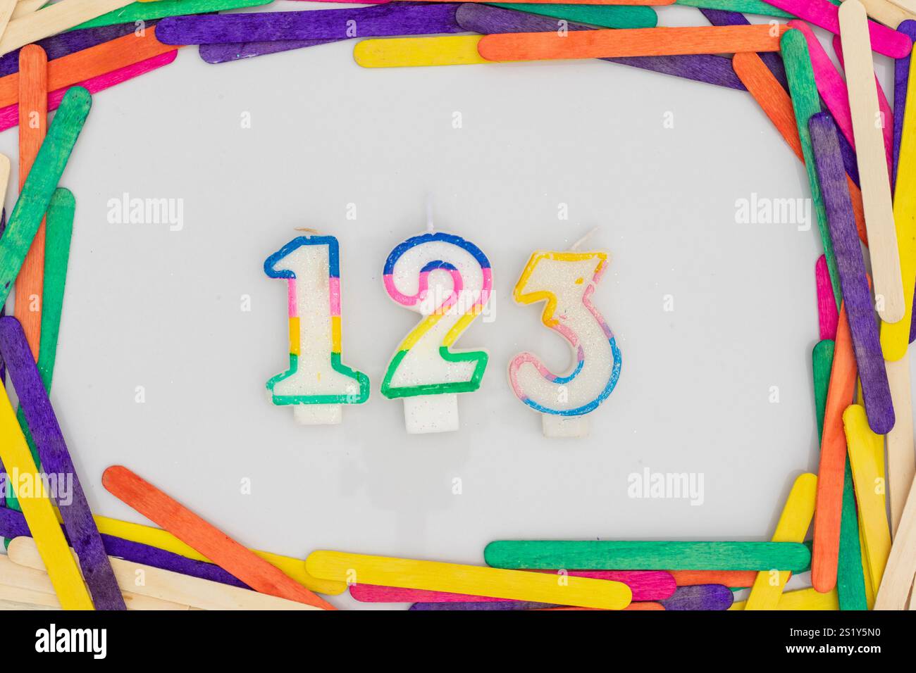 Candles in shape of the number 123 in popsicle colorful sticks frame isolated on white background Stock Photo