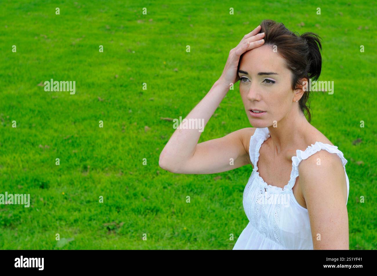 Beautiful young brunette woman with her hand to her head and a worried anxious expression thinking about something. Stock Photo