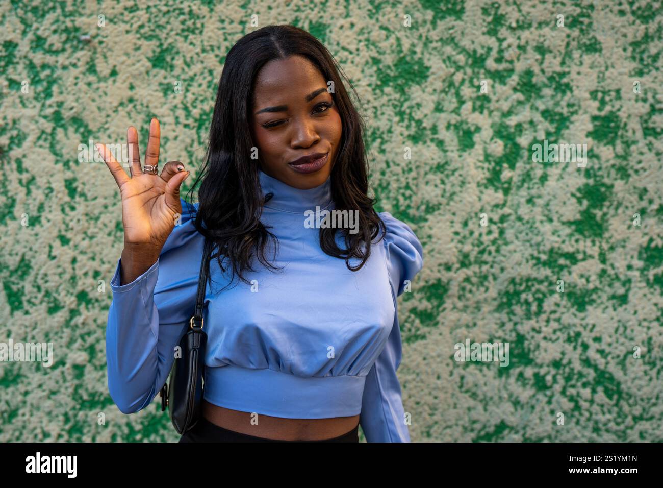 Portrait of a beautiful young black woman winking and gesturing ok sign ...