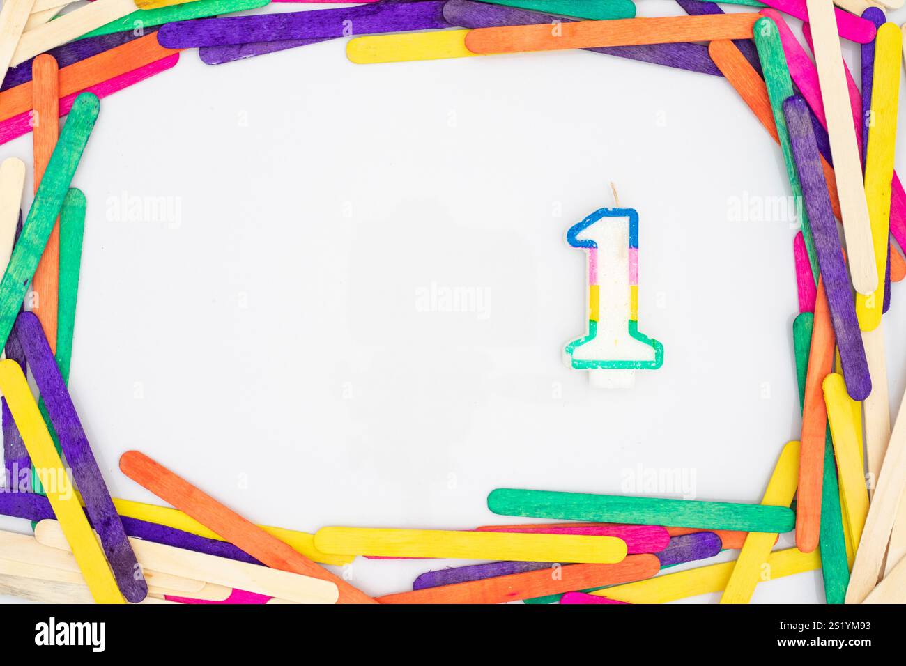 One numerical number shape rainbow colors candle in a colorful wooden sticks frame border on white background with empty space for your text. Stock Photo