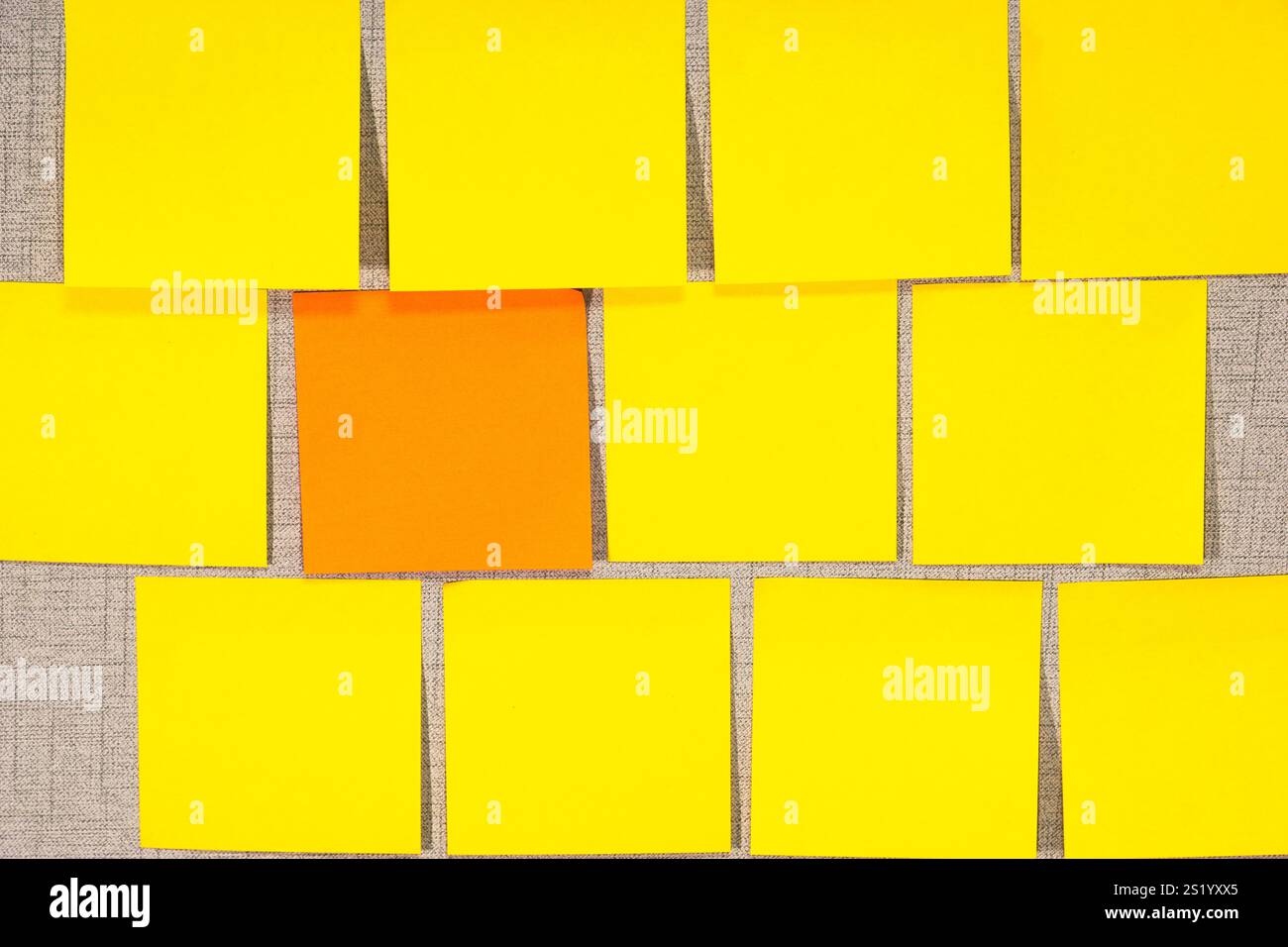 A grey wall covered in empty yellow sticky notes, with one orange Stock Photo