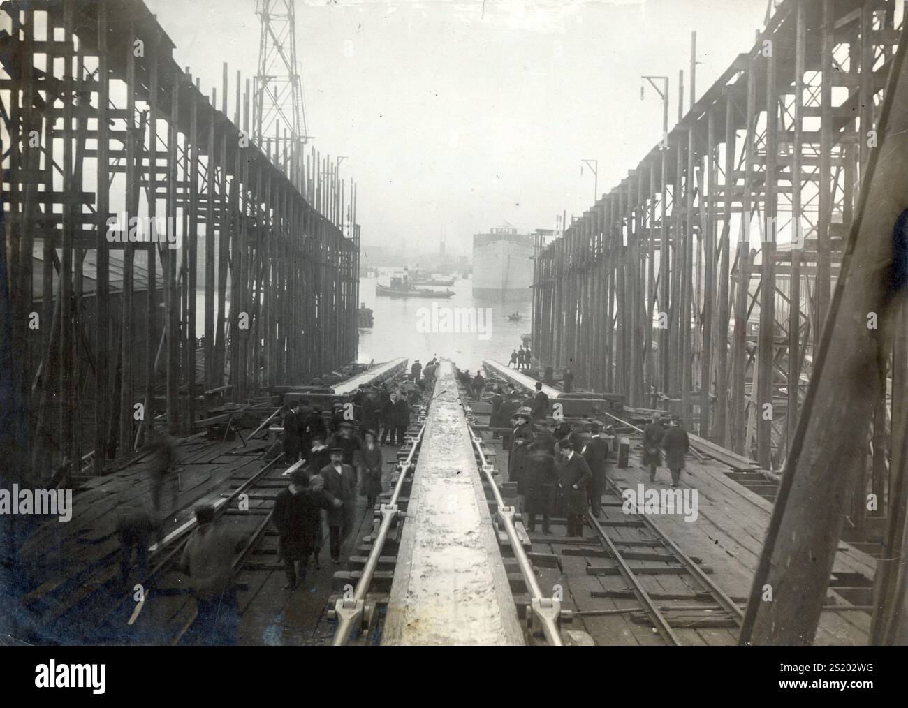 People  at a slipway ina shipyard. In the background a large ship that has probably just been launched. Netherlands, Location unknown, 1911. Stock Photo