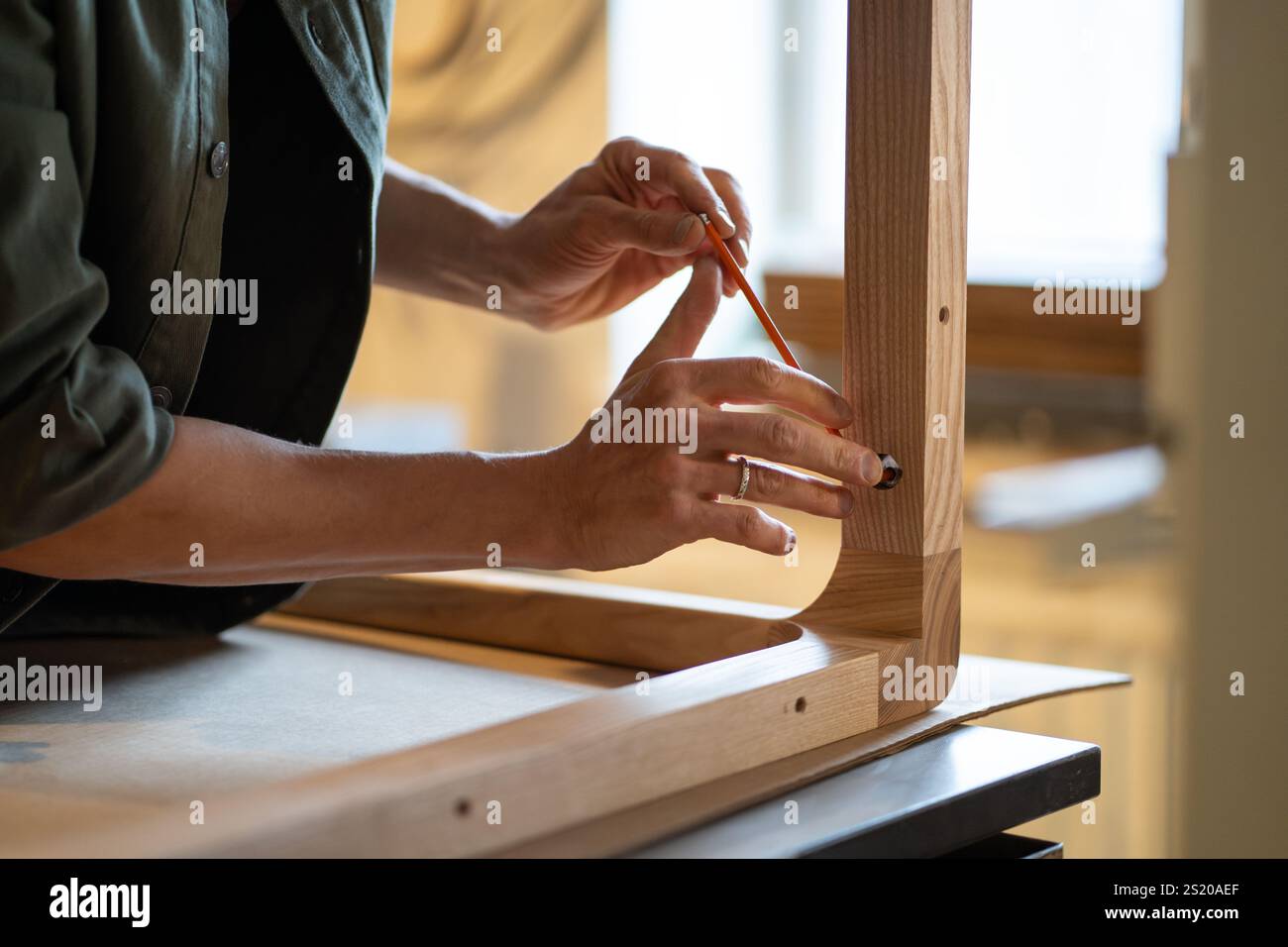 Carpenter hands carefully screw bolts with hex key, securing table legs to woo tabletop in workshop Stock Photo