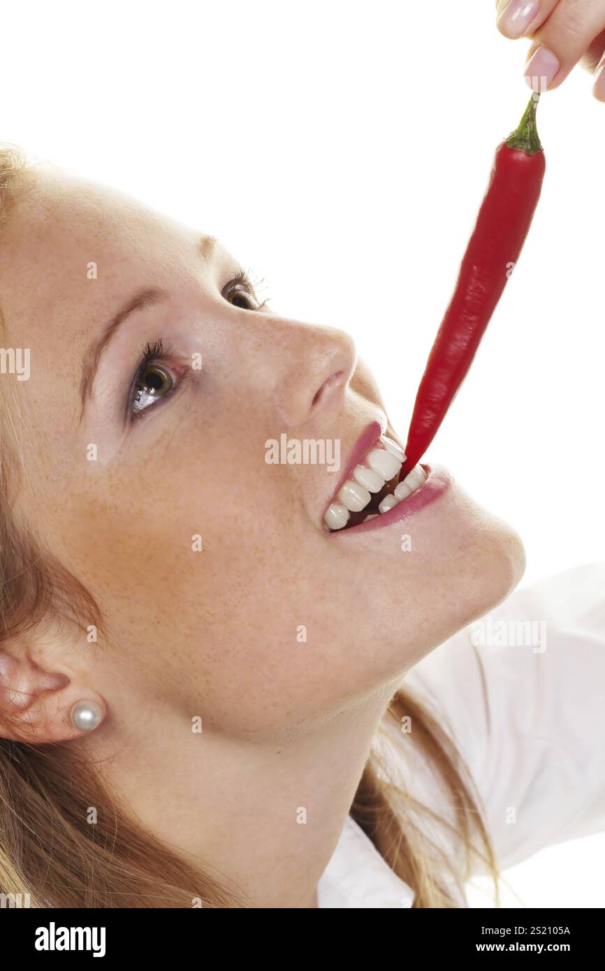 A young woman bites into a chilli pepper. Against a white background Austria Stock Photo