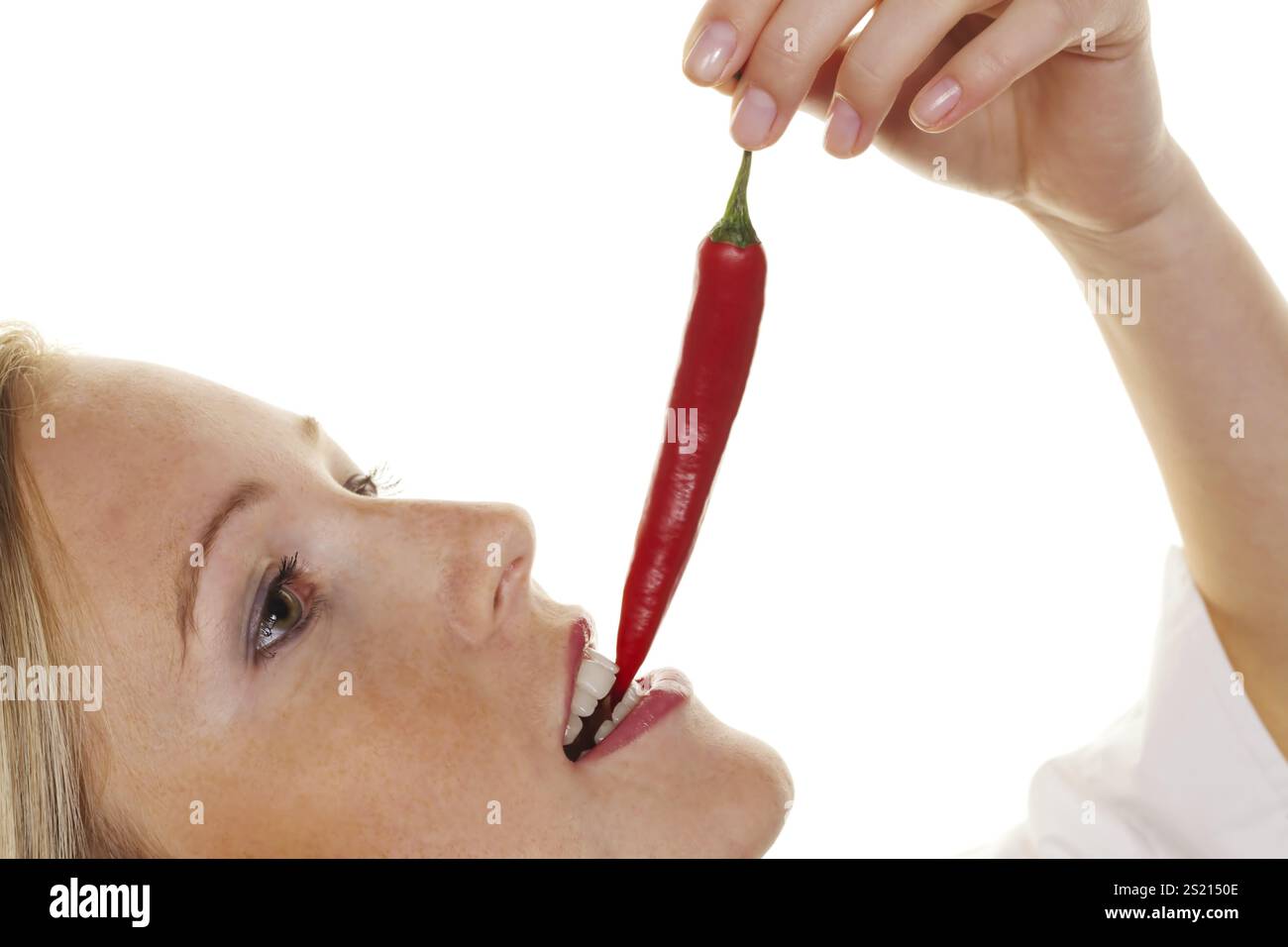 A young woman bites into a chilli pepper. Against a white background Austria Stock Photo