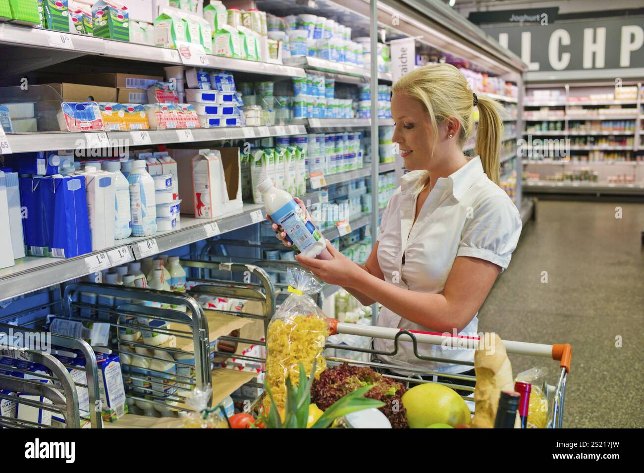 A young woman buys milk in the supermarket. Standing in front of the chiller cabinet. Austria Stock Photo