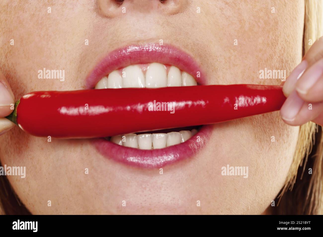 A young woman bites into a chilli pepper. Against a white background Austria Stock Photo