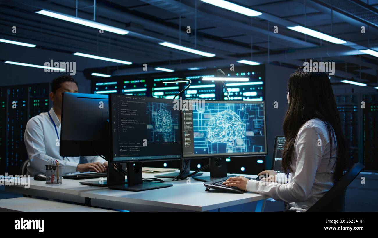 Technicians coworkers using AI tech on computer to do checkup in server room. Teamworking colleagues in data center using artificial intelligence technology to process datasets for training, camera B Stock Photo