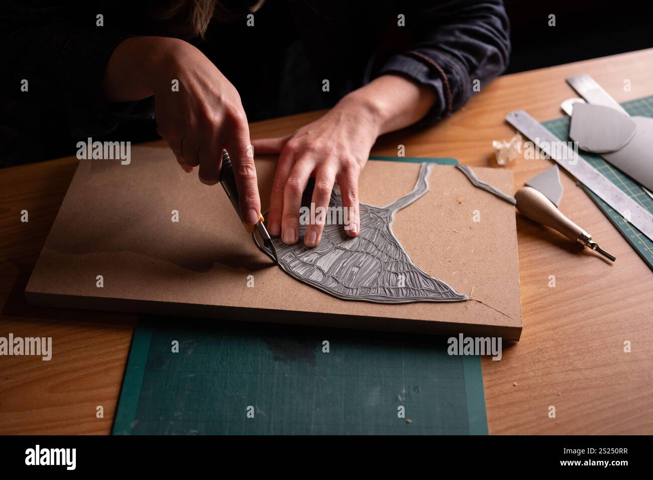 An artist carving a woodcut design for printing. Stock Photo