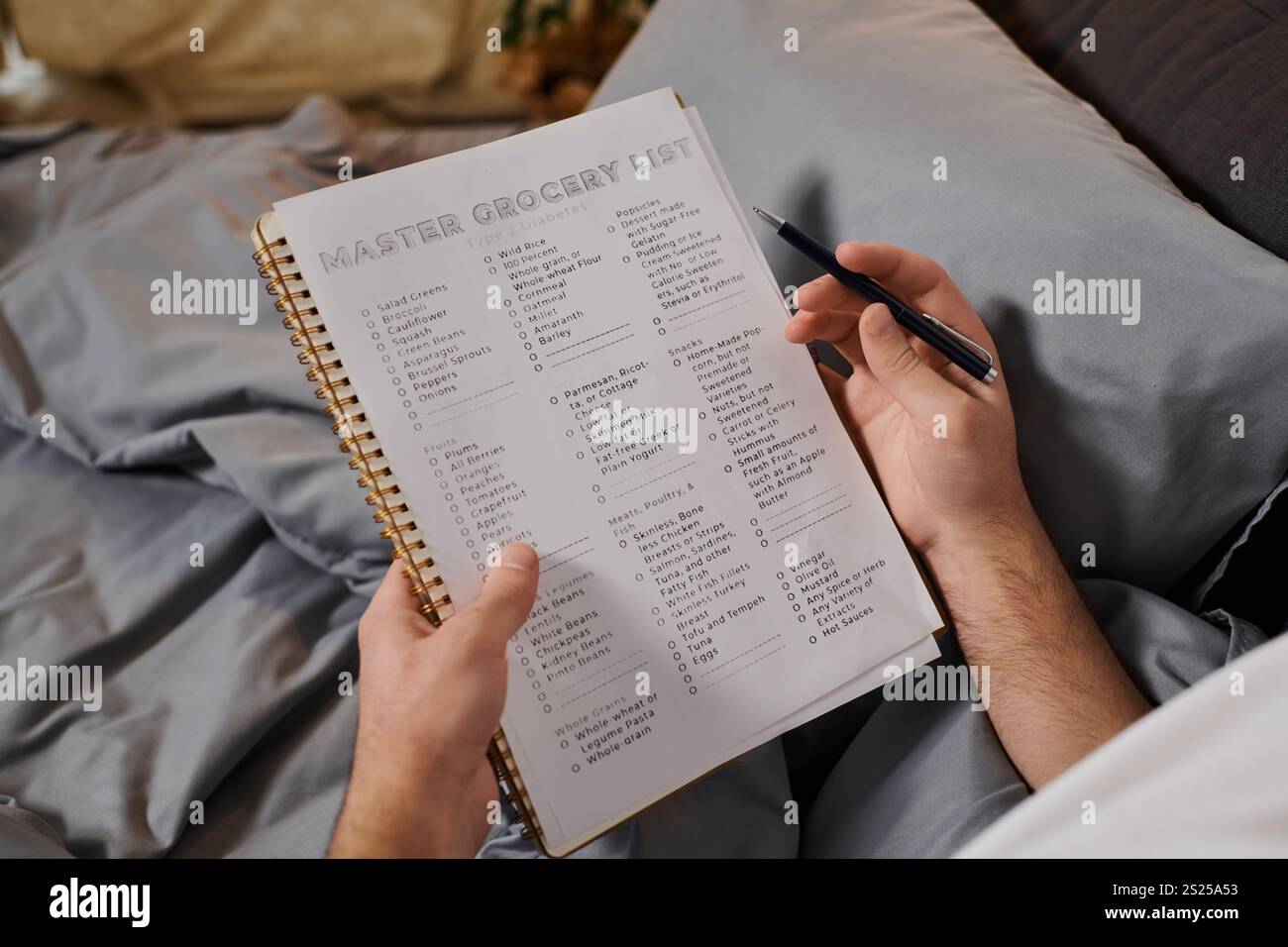 Living with diabetes, a young man writes a grocery list in bed, balancing health and routine. Stock Photo