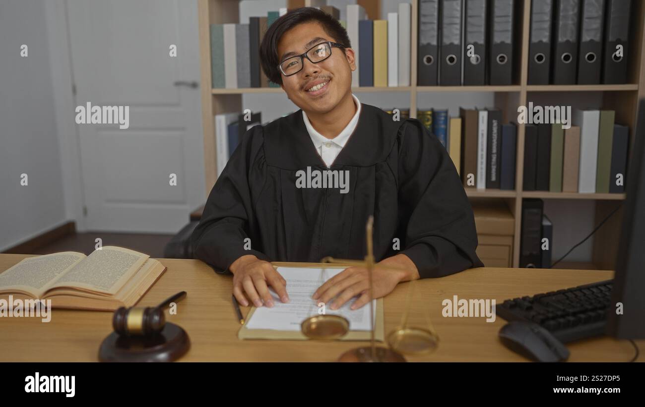 Young chinese man with glasses in a judge's robe at his office desk ...