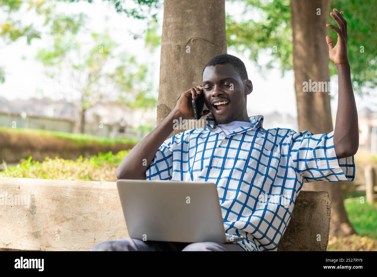 Young cheerful black man using mobile phone and laptop computer. Modern lifestyle Stock Photo