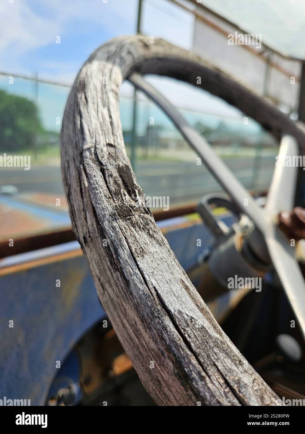 A close-up view of a weathered wooden steering wheel shows the aging wood and the metal center. - Smartphone Captured Stock Image