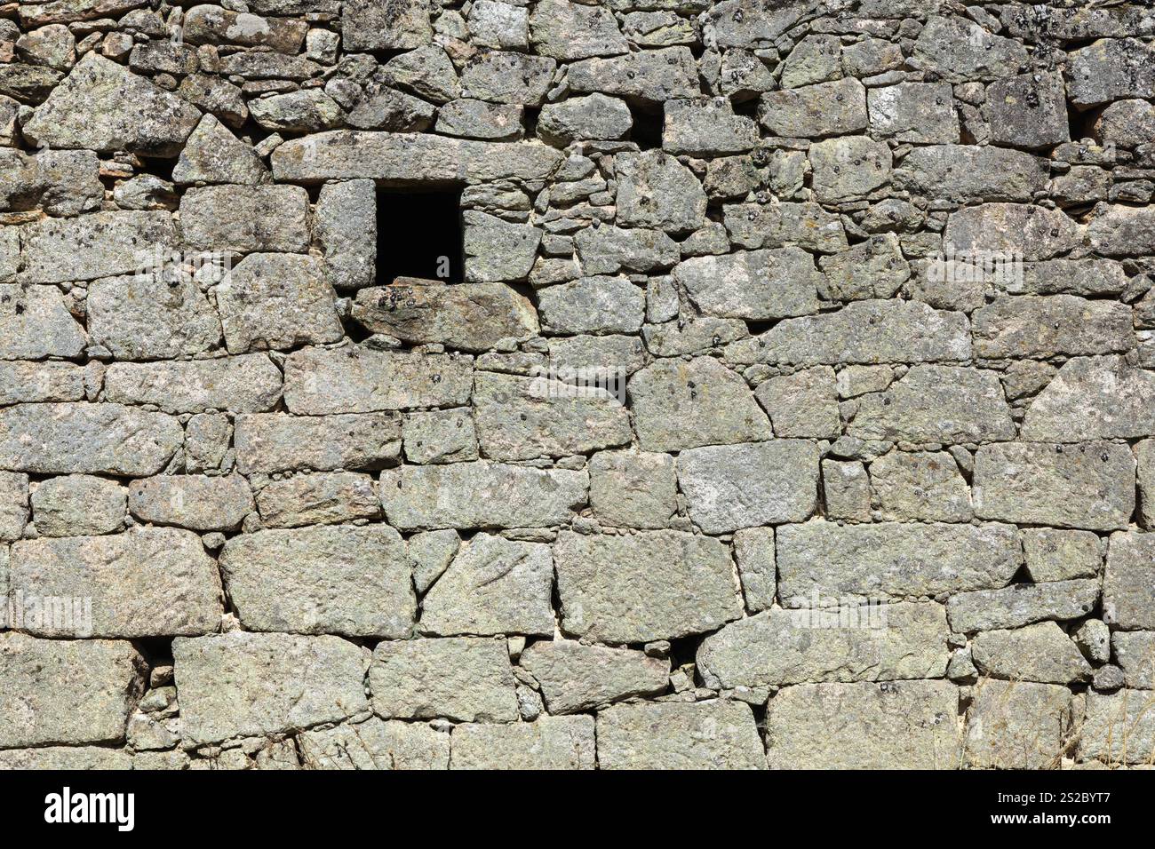 Detail of Side with window of an old abandoned granite detached house with blue sky and tall grass. Stock Photo