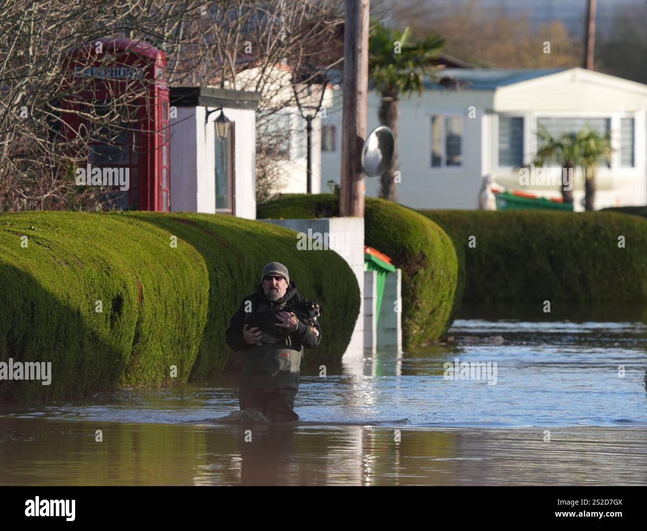 A man wearing waders carries a dog at The Little Venice caravan park in ...