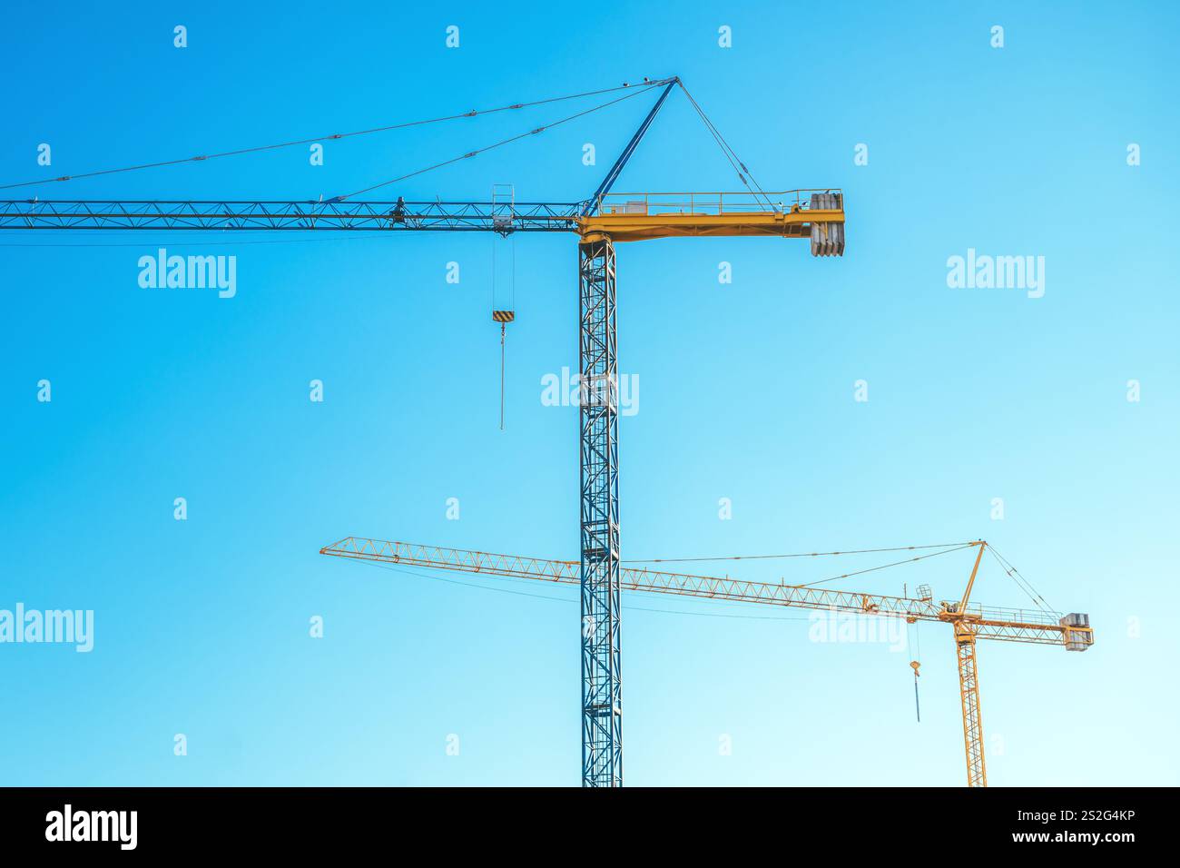 Two construction cranes against blue sky at construction site, selective focus Stock Photo