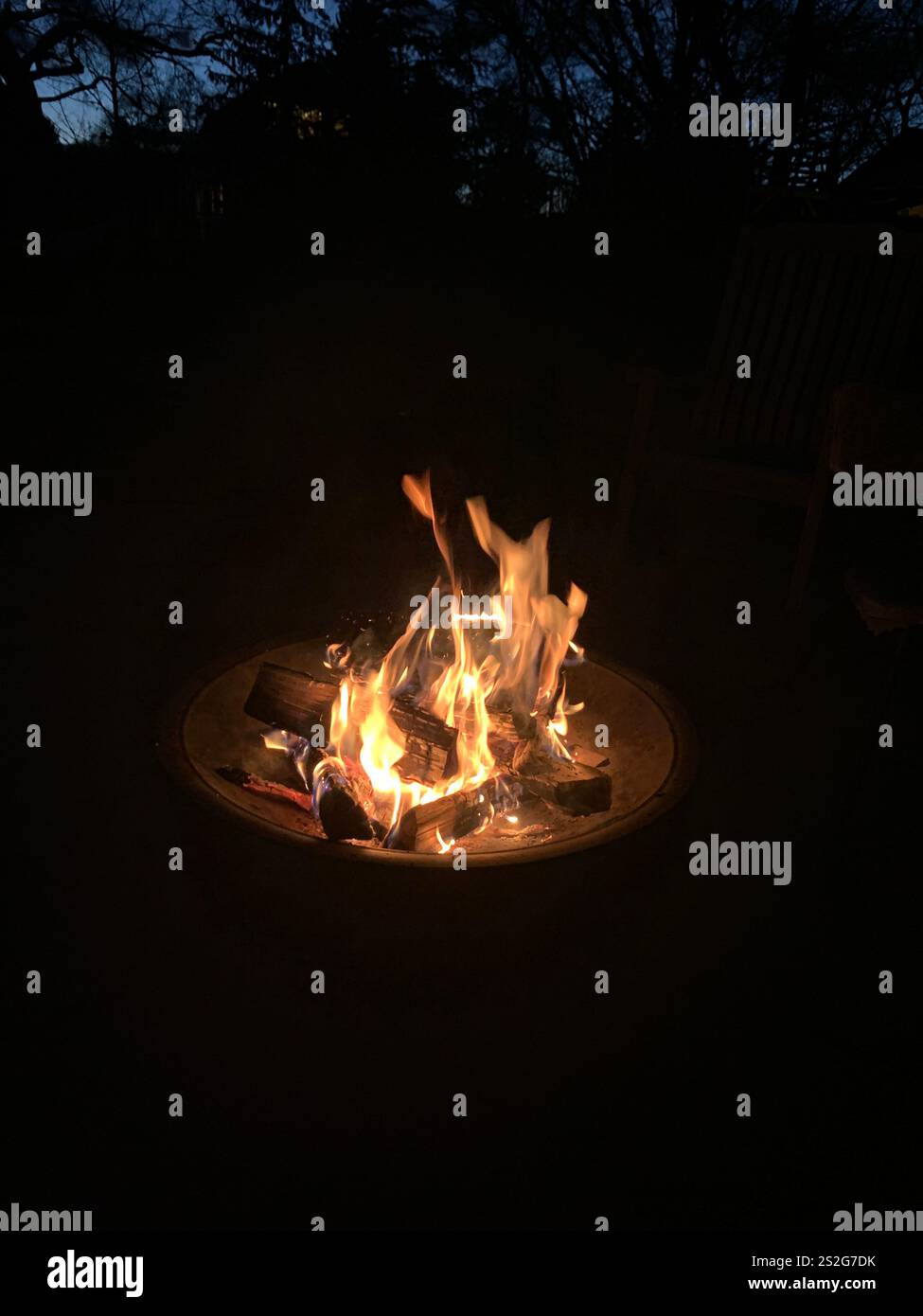 Glowing bonfire with vibrant flames and embers illuminating the night, creating a cozy and atmospheric outdoor gathering spot. - Smartphone Captured Stock Image