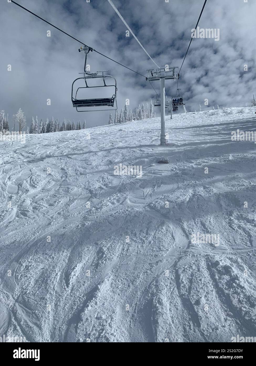 Snow-covered ski slope with fresh tracks and a chairlift under a partly cloudy sky, capturing a classic winter adventure scene. - Smartphone Captured Stock Image