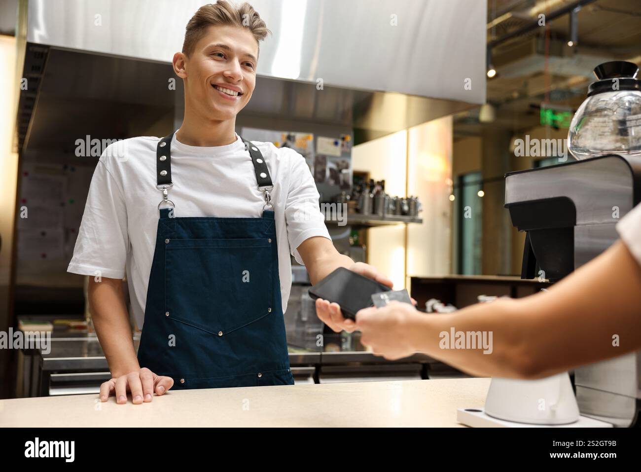Cafe worker taking payment from client via terminal indoors Stock Photo ...