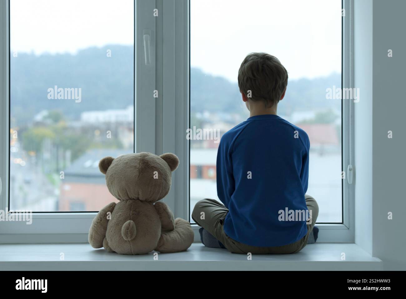 Autism concept. Lonely little boy with teddy bear near window at home ...