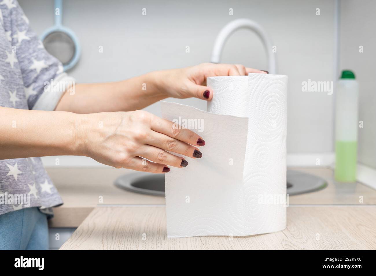 woman's hand ripping off paper towel in kitchen. housewife uses paper towel. roll of paper towel in the kitchen. kitchen cleaning. High quality photo Stock Photo