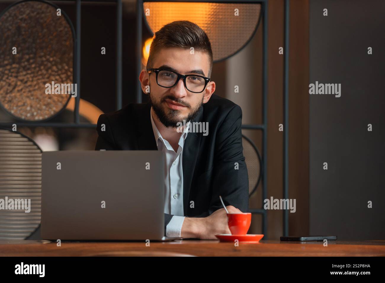 Portrait of young happy business man sitting at his desk in the office ...