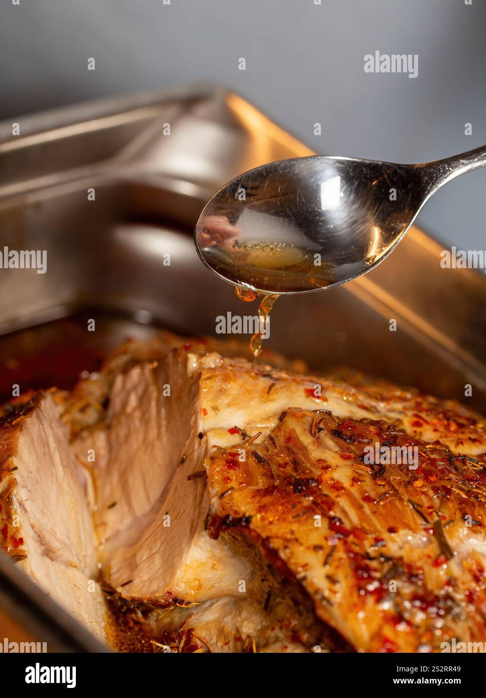 Herb-crusted roasted pork is basted with rich meat juice, showcasing its golden, flavourful crust and enhancing rich rosemary seasoning. Stock Photo