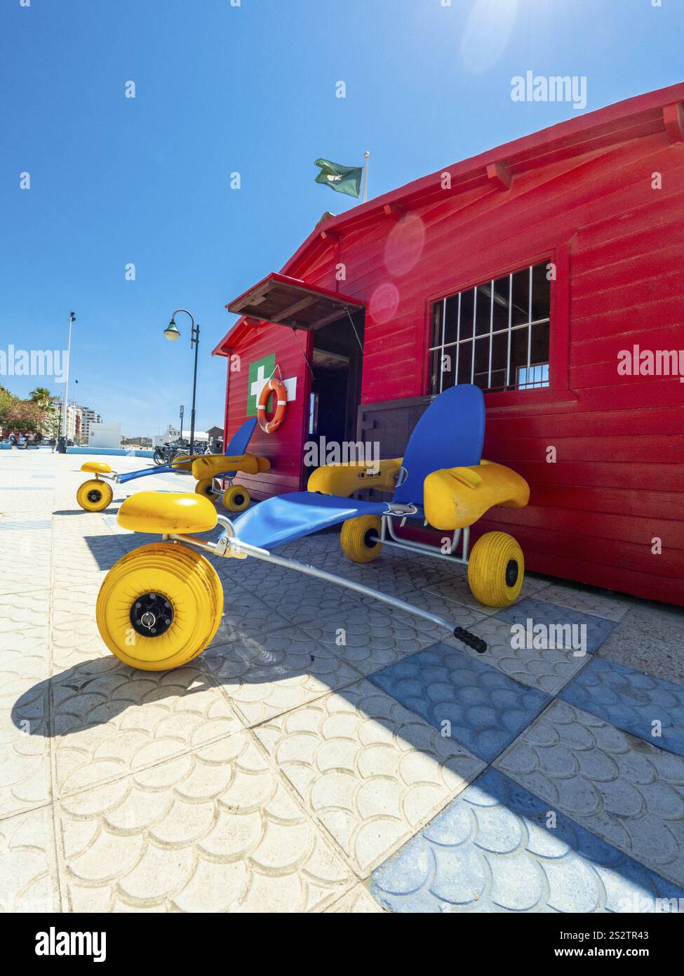 Floating wheelchairs parked near a red lifeguard station on a sunny summer beach, promoting accessibility and inclusion for people with disabilities Stock Photo