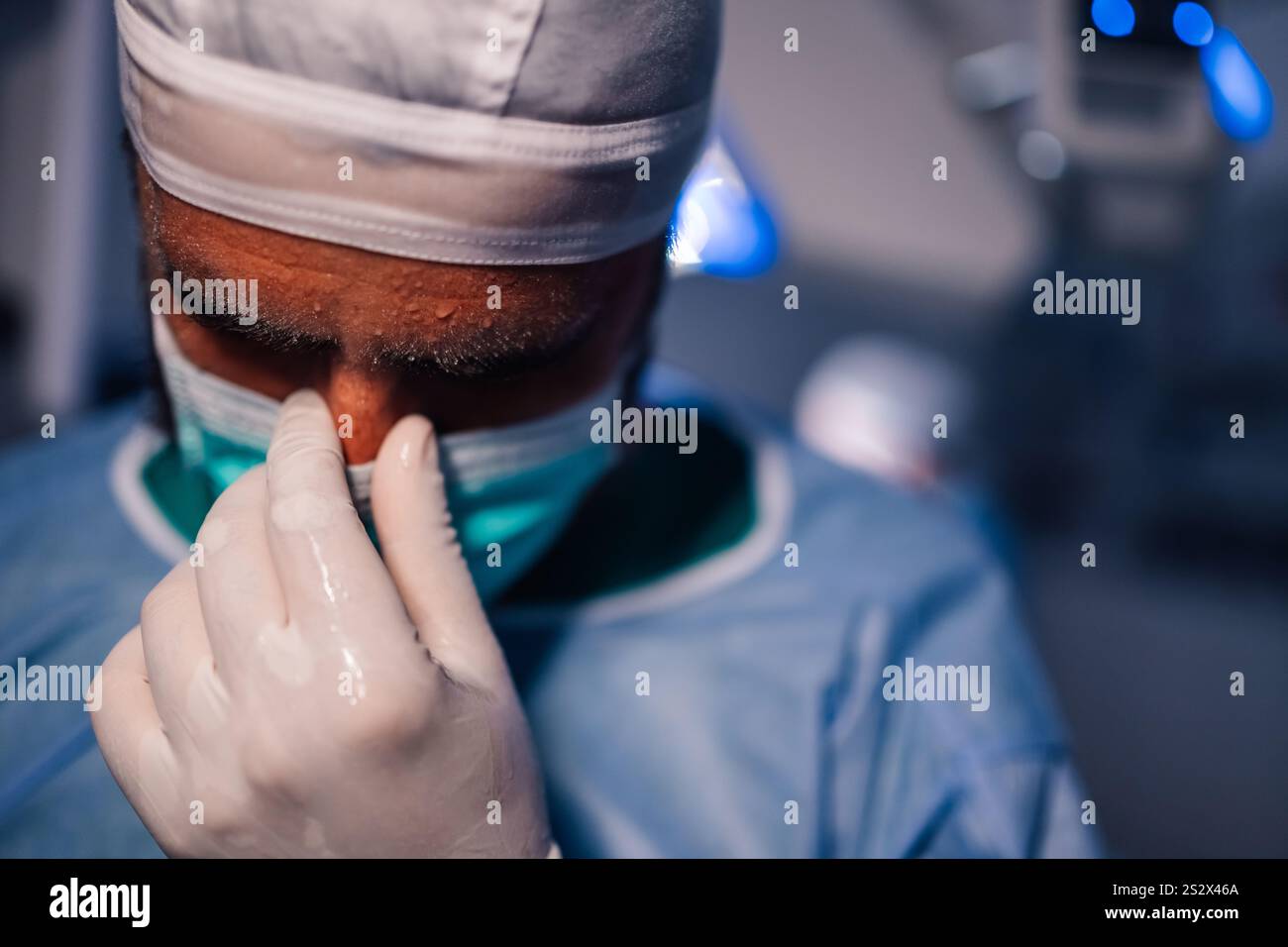 A surgeon in a modern operating room adjusts his mask with intense focus, embodying the dedication and precision required in the medical profession. B Stock Photo