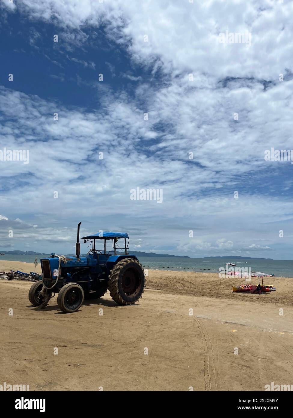 A vertical shot of a beach, a blue tractor, sky and ocean - Smartphone Captured Stock Image