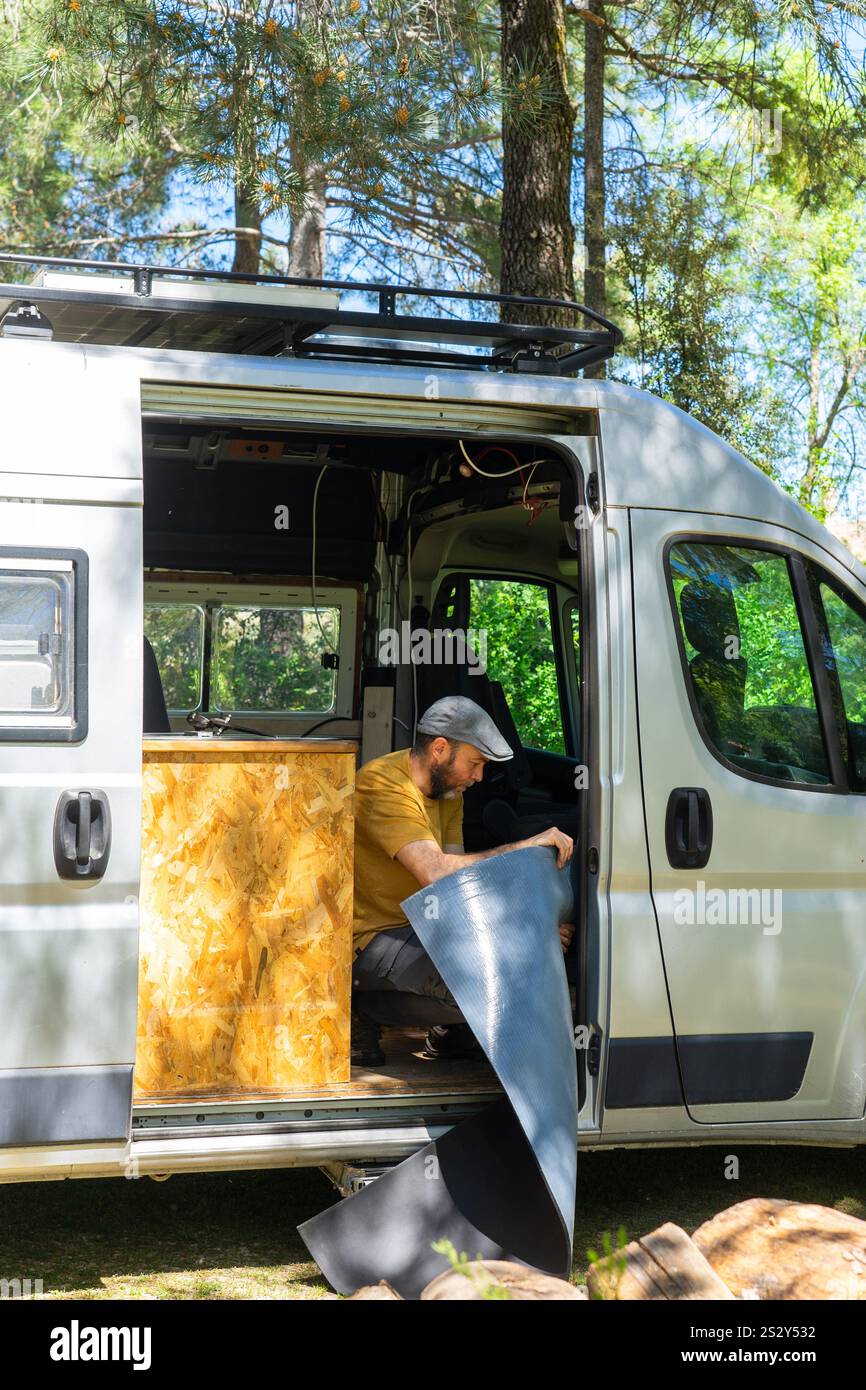 Concentrated man installing insulation material inside his campervan during a conversion process in a forest Stock Photo