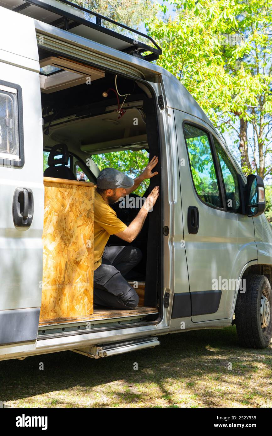 Carpenter installing mosquito net on a van door, converting a van into a camper Stock Photo