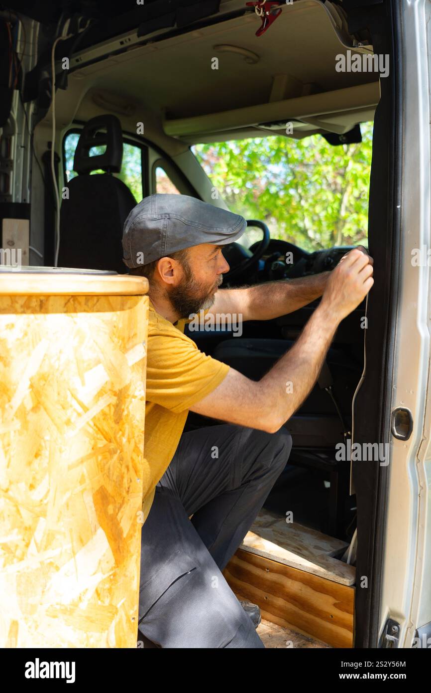 Carpenter working inside a camper van, installing insulation on the door Stock Photo