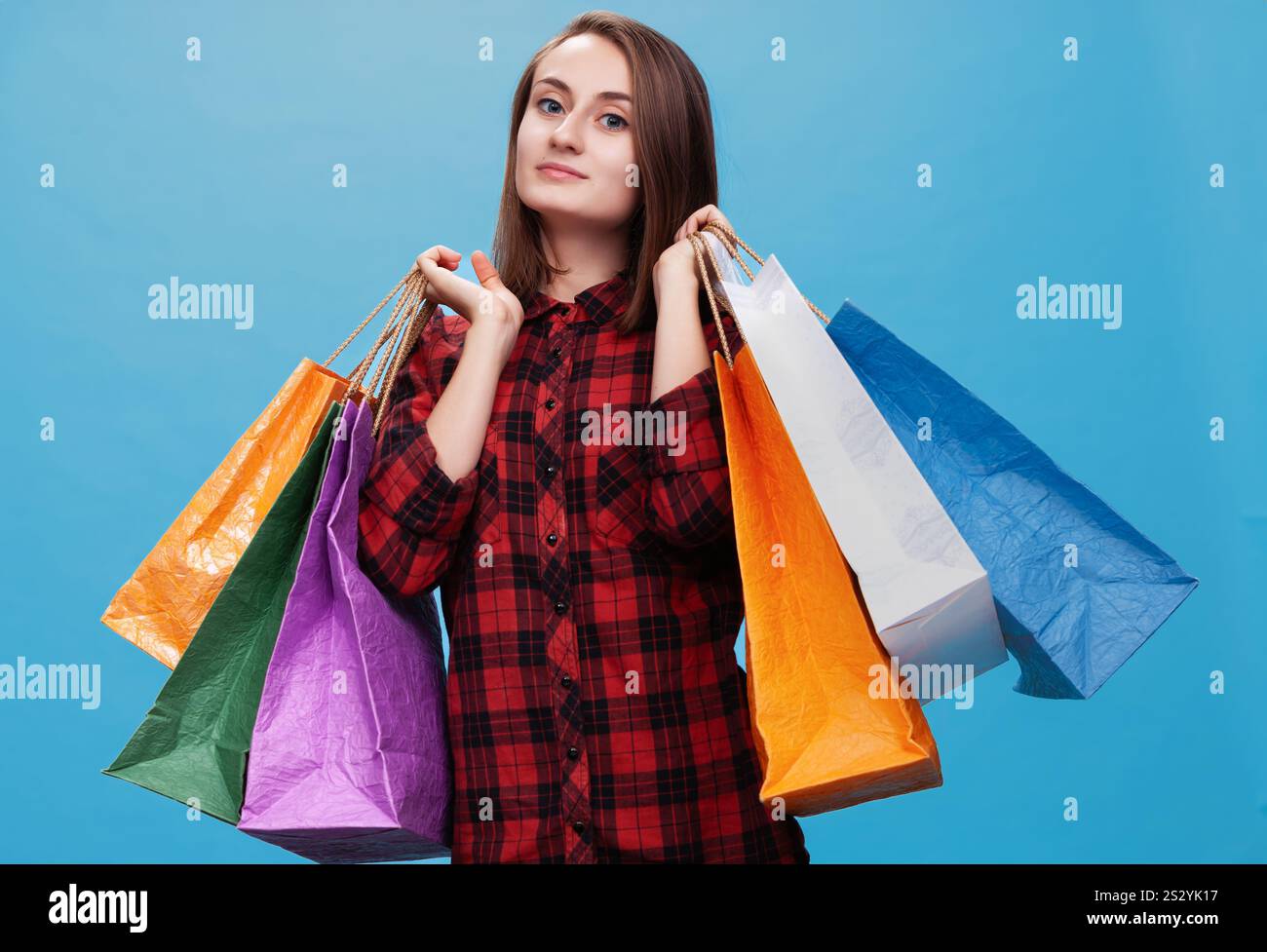 A happy young woman poses confidently with multiple colorful shopping bags. Stock Photo