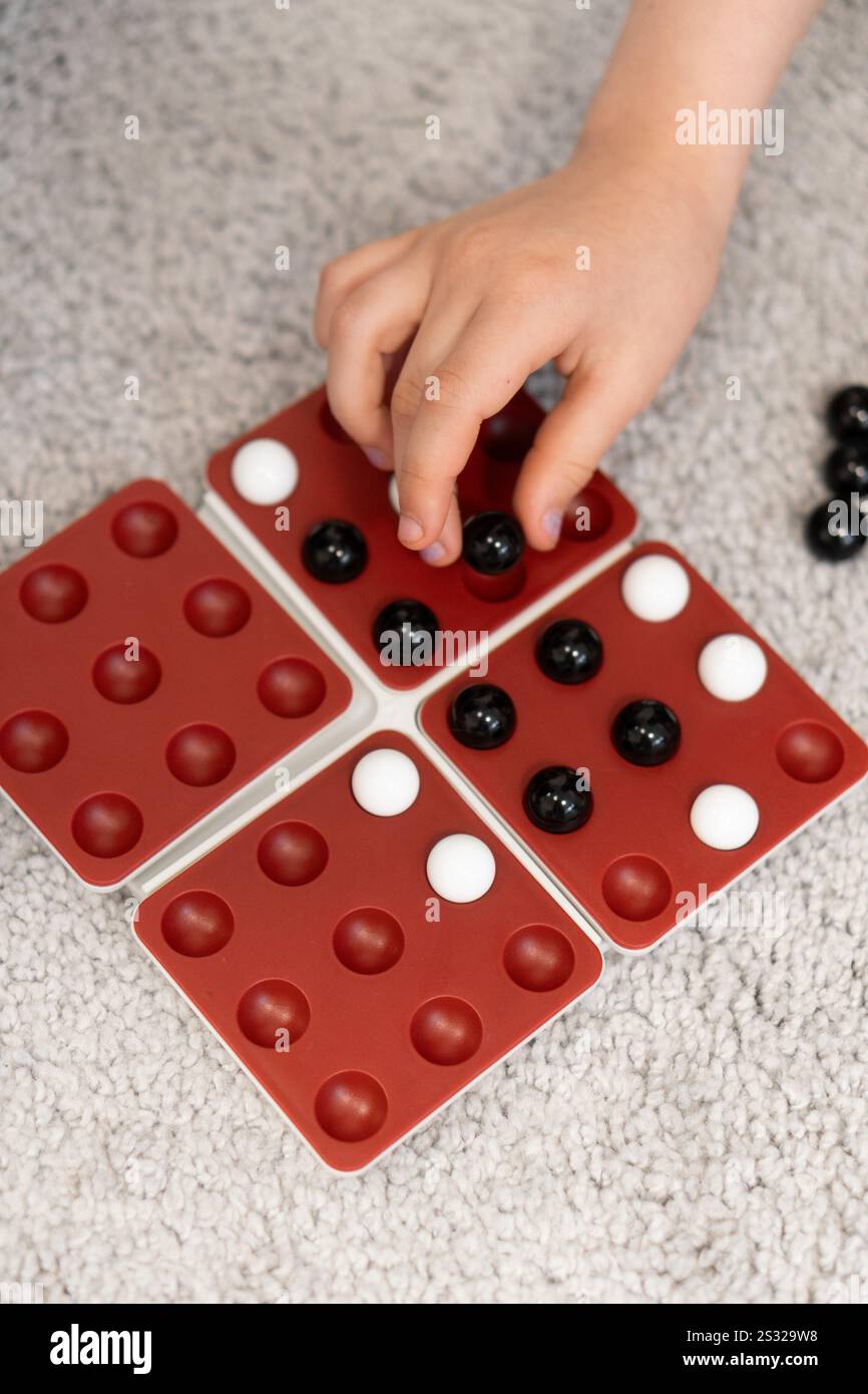 Children's hands move marbles on the game board, adjusting their strategy with each turn. The game is a fun test of skill and planning. Stock Photo