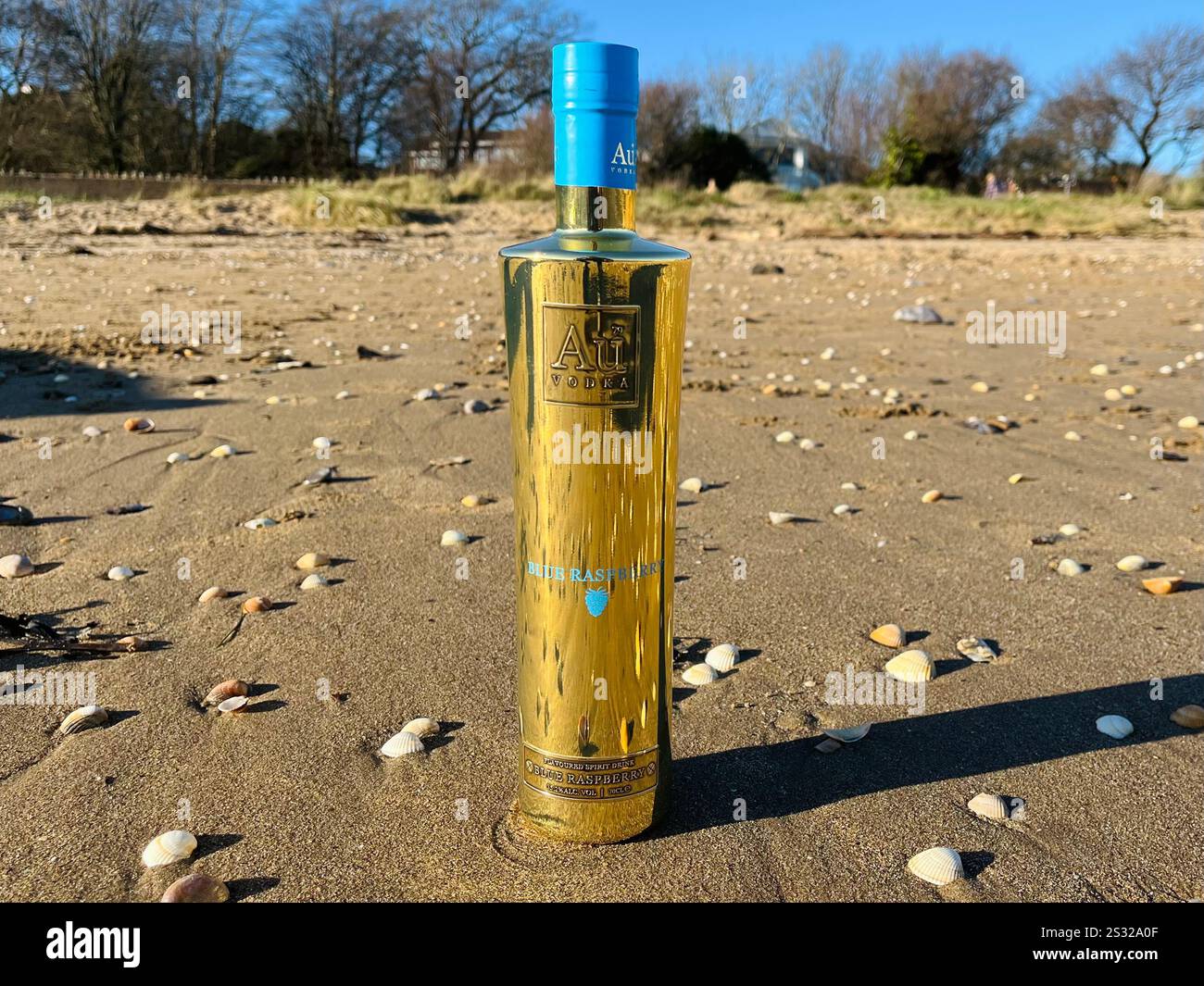Au Vodka Blue Raspberry bottle on the sands of Swansea Bay. The Swansea-based company is known for their iconic gold bottles and ultra-premium vodka. Stock Photo