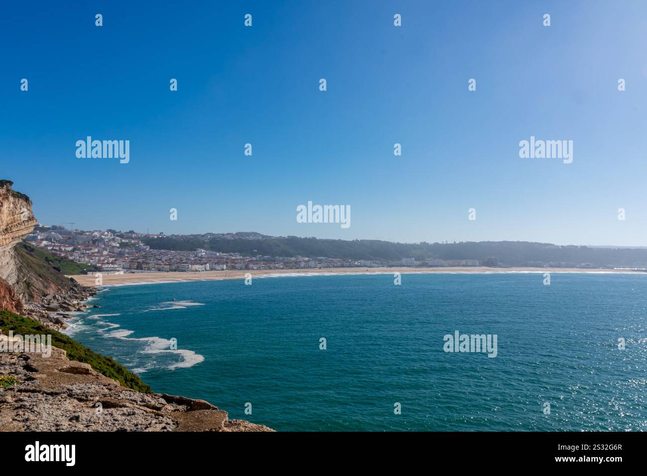 Nazaré, Portugal - An expansive sandy beach meets turquoise Atlantic waves under a bright, clear sky. Stock Photo