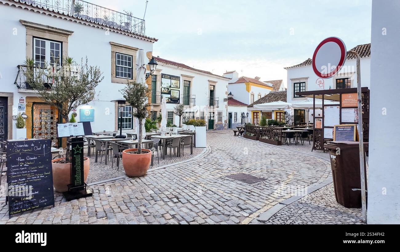 A street in Faro, Portugal, lined with restaurant outdoor patio seating on both sides, currently empty with no tourists due to the winter low season Stock Photo