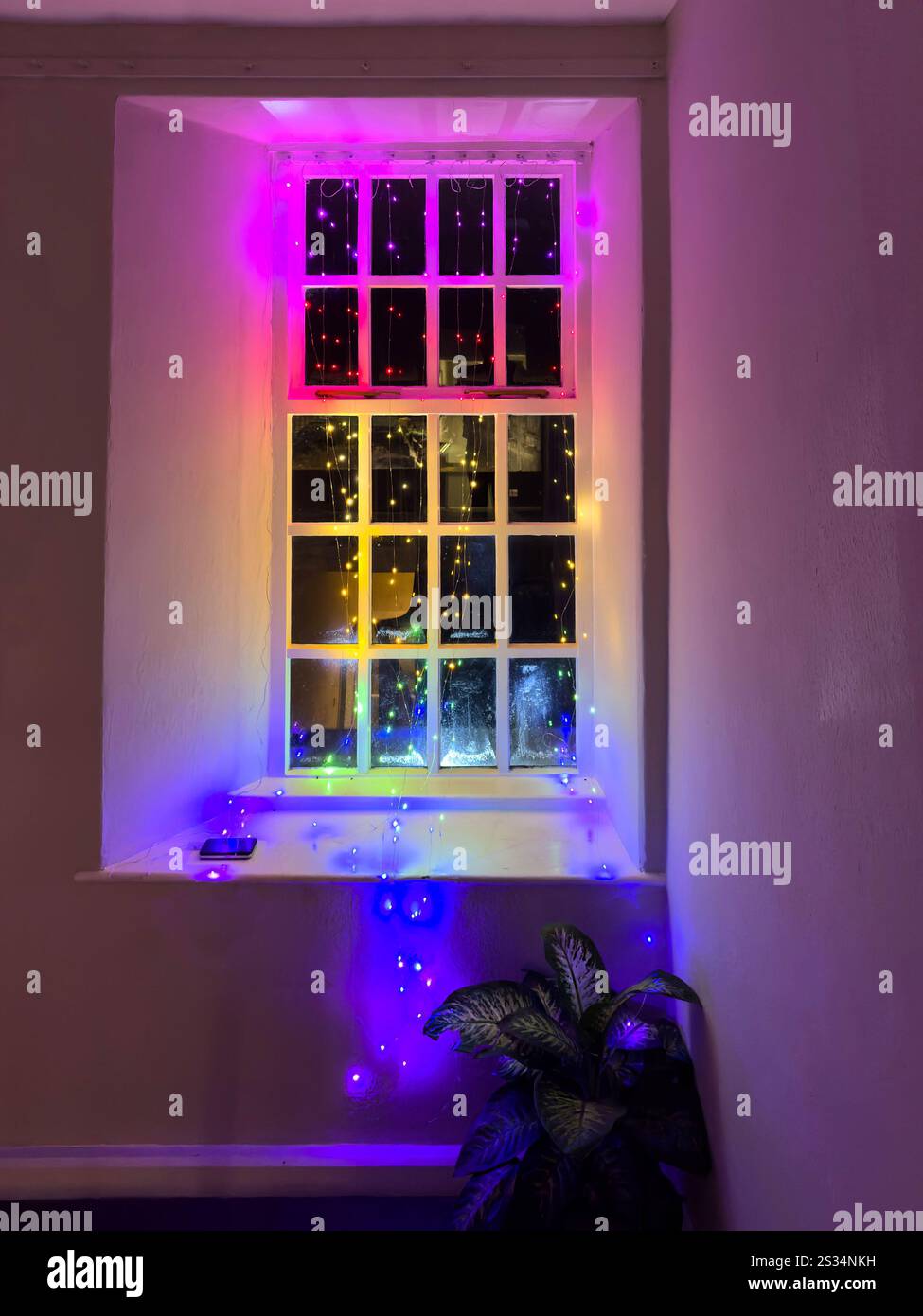 rainbow coloured christmas lights on the inside of an old georgian traditional farmhouse sash window - Smartphone Captured Stock Image