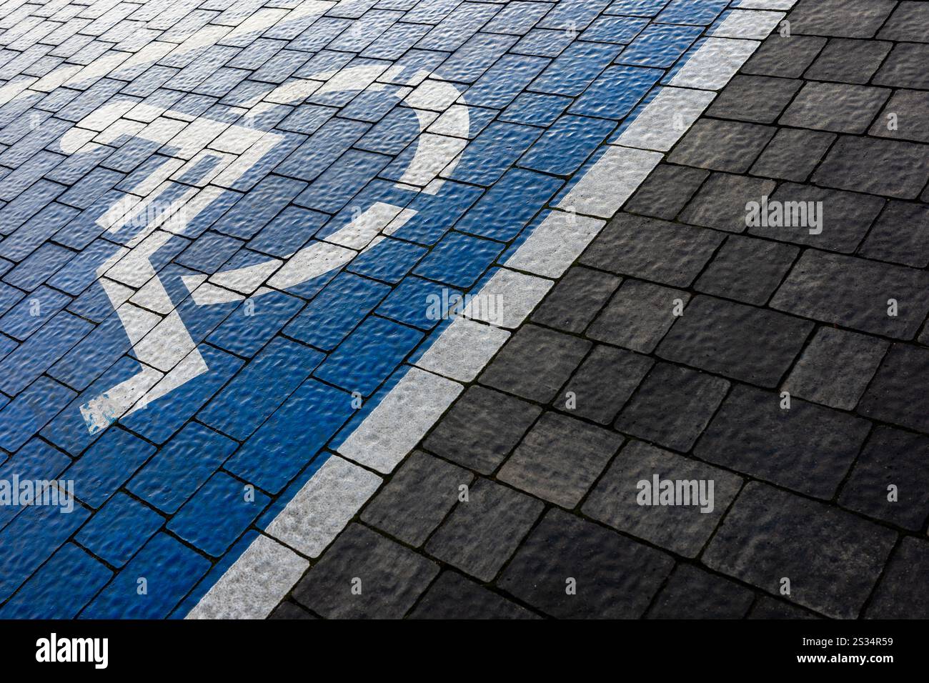 White and blue marking of a disabled parking space in a parking lot made of gray blocks. A drawing of a wheelchair painted on the surface. Stock Photo