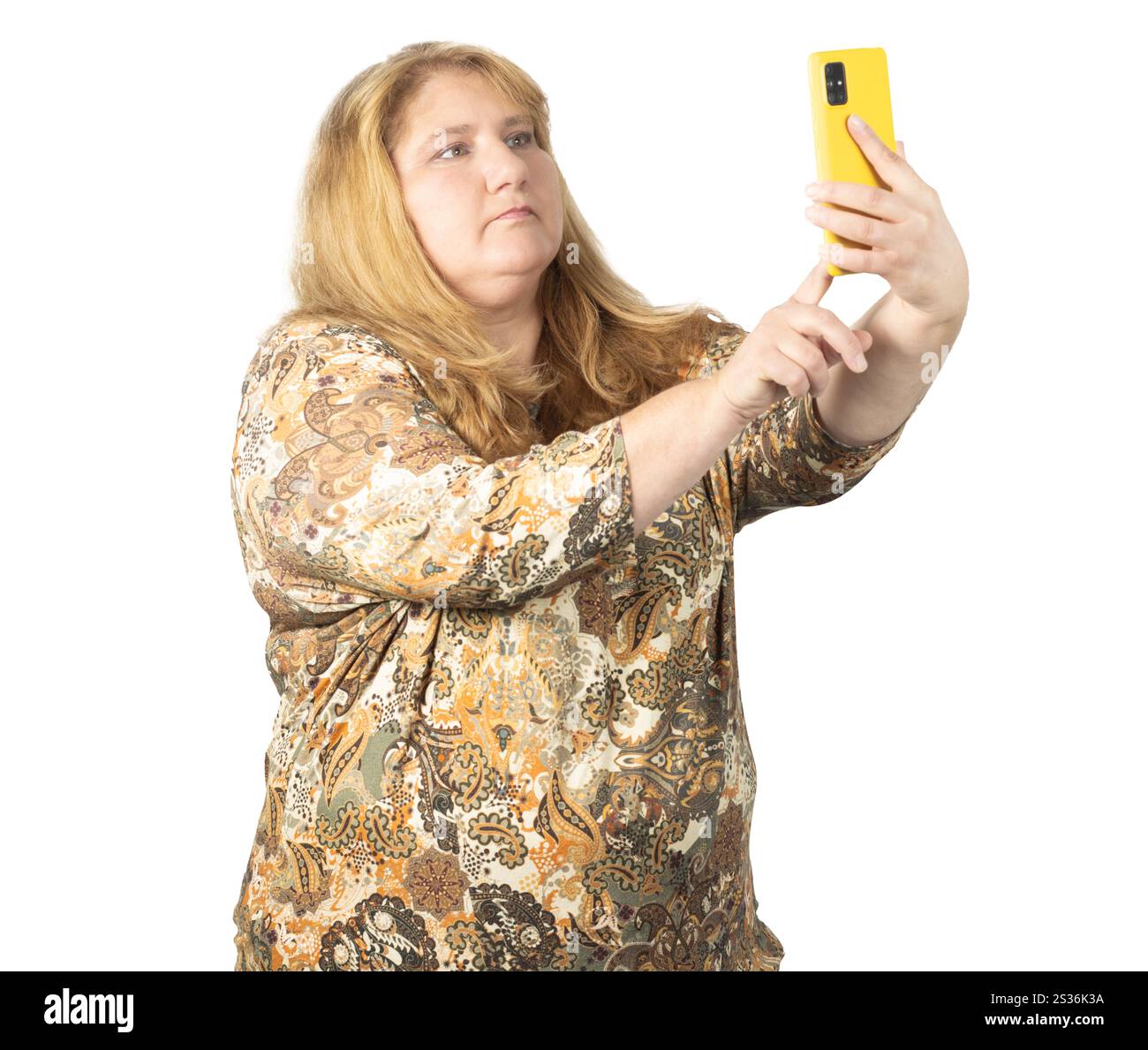 A woman with long blonde hair wearing a patterned blouse holds a smartphone while taking a selfie. Stock Photo