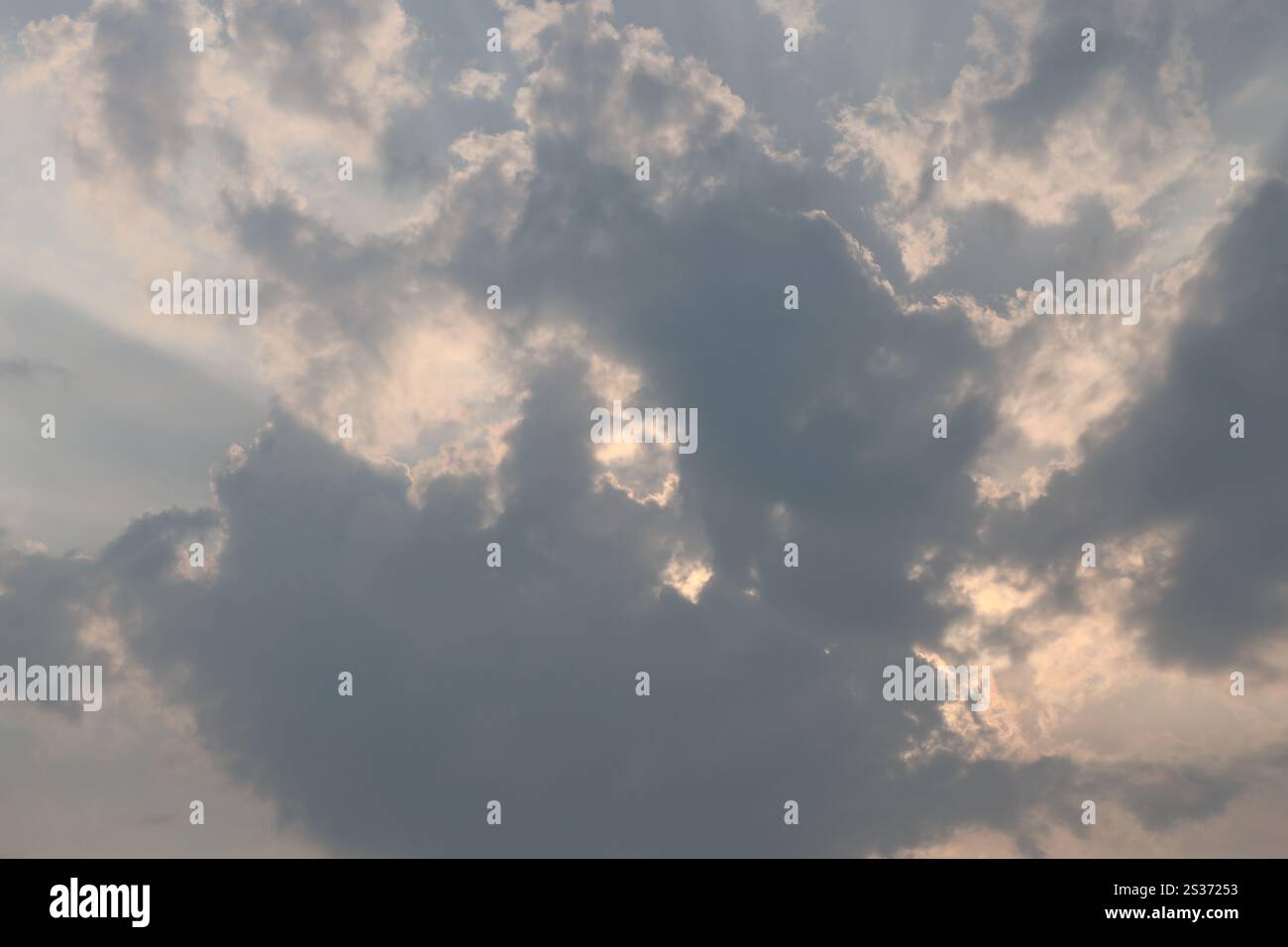 sunlight streaming across high clouds from behind lower dark clouds Stock Photo