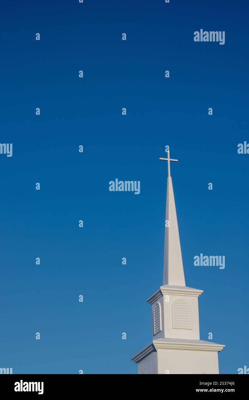 A white church steeple with a cross at its peak stands tall against a ...