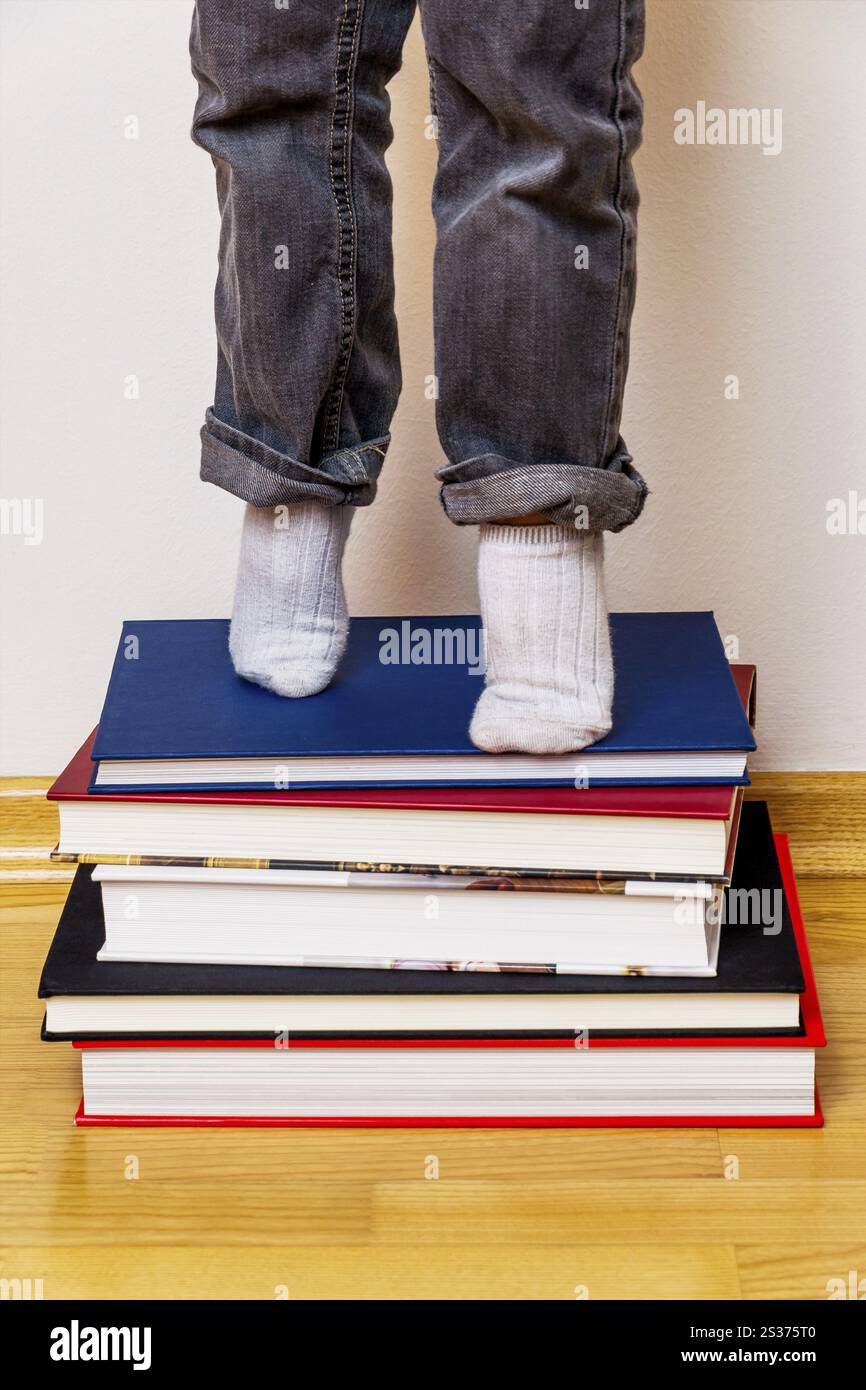 Child standing on a pile of books, symbolising school education, reading skills, learning support Stock Photo