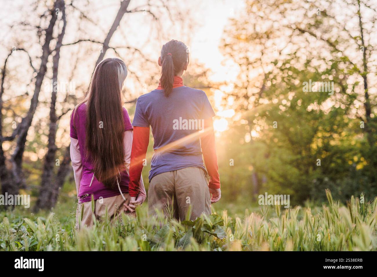 Two women holding hands enjoying a walk in nature at sunset, embracing ...