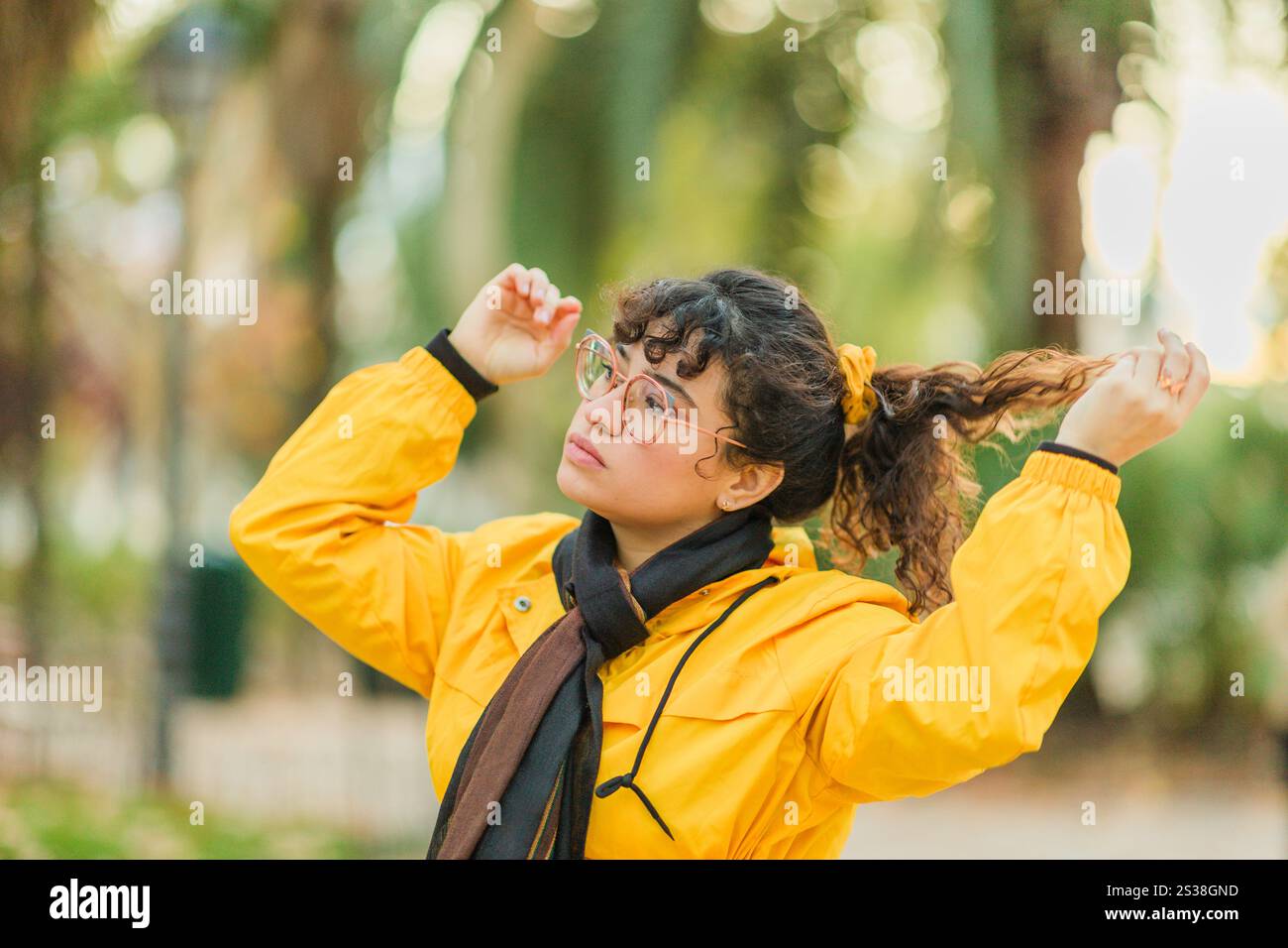 Young woman wearing yellow jacket touching her hair in a park Stock ...