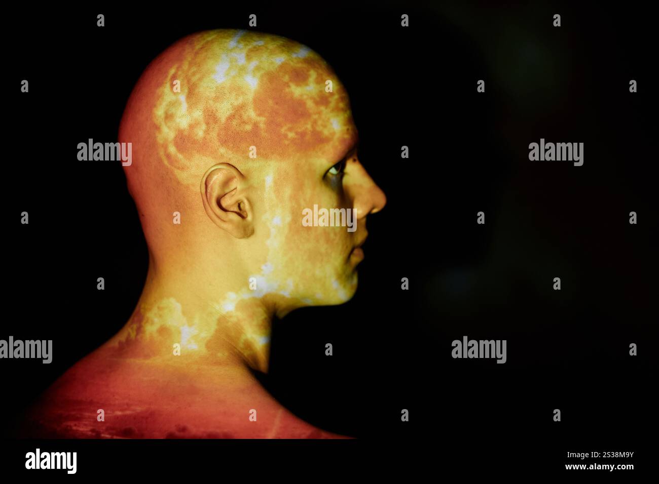 Profile shot of emotionless bald man with image of nuclear explosion flame projected onto face posing against black background in studio, copy space Stock Photo