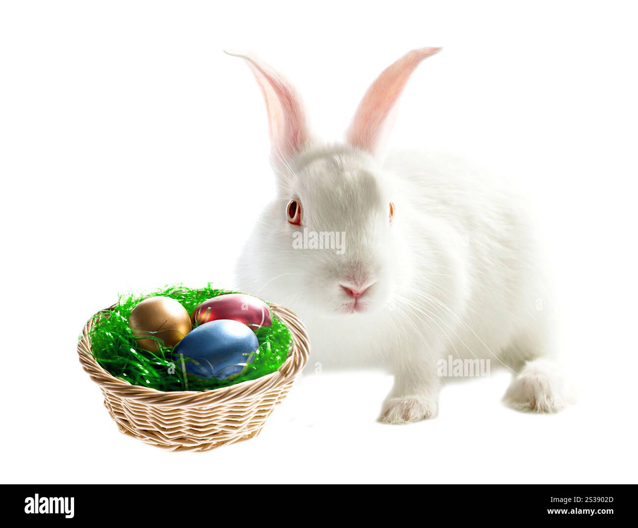 White easter bunny next to a basket filled with colorful eggs on a ...